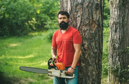 Firewood as a renewable energy source. Lumberjack worker with chainsaw in the forest. Deforestation. The Lumberjack working in a forest. Professional lumberjack holding chainsaw in the forest