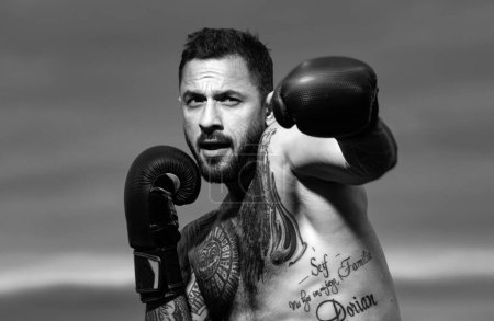 Téléchargez les photos : Boxer in a fight. Fist fight. Strong man with tattooed body boxing outdoor. Man with muscular body and bare torso with boxing punch gloves. Boxing training outside - en image libre de droit