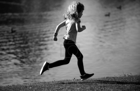 Photo for Child boy running outdoors. Kid running in a summer park. Kids running on green meadow against sea or lake - Royalty Free Image
