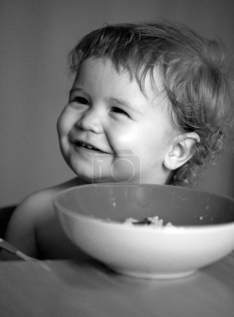 Photo for Portrait of cute Caucasian child kid with spoon. Hungry messy baby with plate after eating puree - Royalty Free Image