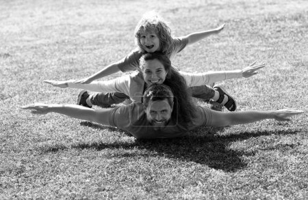 Foto de Familia acostada en el césped en el parque. Concepto de mosca, niño pequeño está sentado pickaback mientras imita el vuelo - Imagen libre de derechos