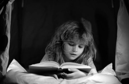 Téléchargez les photos : Un livre pour enfants. C'est l'heure du coucher. Garçon lisant un livre au lit - en image libre de droit