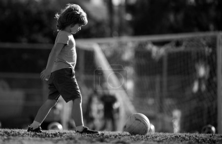 Foto de Niño jugador de fútbol pateando fútbol en el campo de deportes. Niños activos. Fútbol infantil. Juegos de pelota activa - Imagen libre de derechos