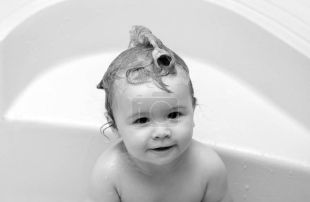 Foto de Baño infantil. Divertido bebé feliz se baña en la bañera con agua y espuma. Higiene infantil. Niños divertidos se enfrentan de cerca - Imagen libre de derechos