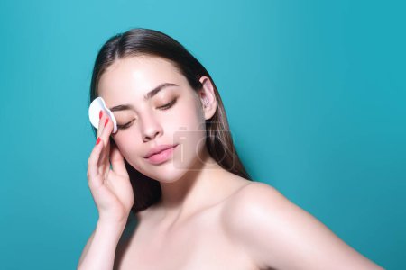 Téléchargez les photos : Woman cleansing skin by cotton pad sponge. Spa and wellness, skin care. Beauty routine. Beautiful girl cleaning face with cotton pad. Skin treatment, cosmetology - en image libre de droit