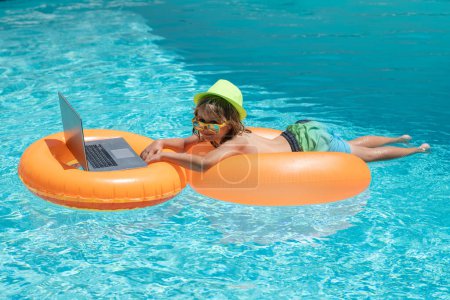 Photo for Little business man in summer vacation trip. Kid working on laptop computer at poolside swimming pool. Summer online technology. Traveler relaxing on tropical sea in summer holidays - Royalty Free Image