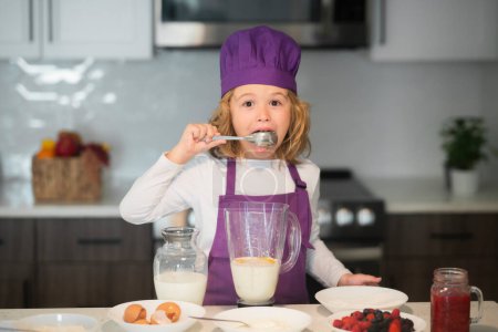 Téléchargez les photos : Préparation saine des repas et du dîner. Chef cuisinier enfant cuisson sur la cuisine, lécher la cuillère - en image libre de droit