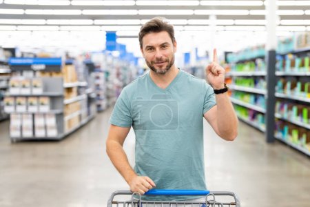 Photo for Handsome man with shopping basket with shopping trolley at grocery. Man buying groceries in supermarket. Male model in shop. Concept of shopping at supermarket - Royalty Free Image