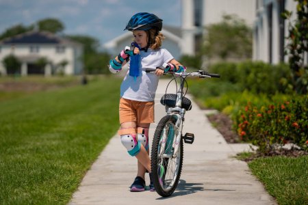 Photo for Child riding a bike in summer park. Children learning to drive a bicycle on a driveway outside. Kid riding bikes in the city wearing helmets as protective gear. Child on bicycle, bike outdoor - Royalty Free Image