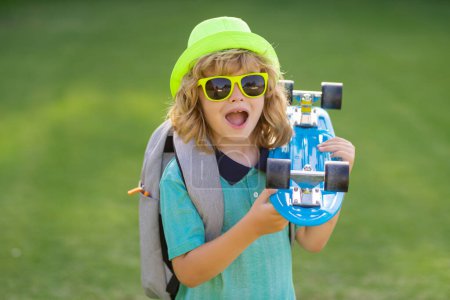 Photo for Excited child. Skateboarder child boy in skate park. Kid boy with skateboard. Childhood, leasure, lifestyle concept. Portrait stylish child with skateboard outdoors - Royalty Free Image