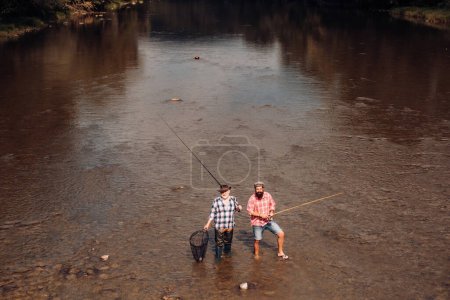 Photo for Two men friends fishing. Flyfishing angler makes cast, standing in river water. Old and young fisherman - Royalty Free Image