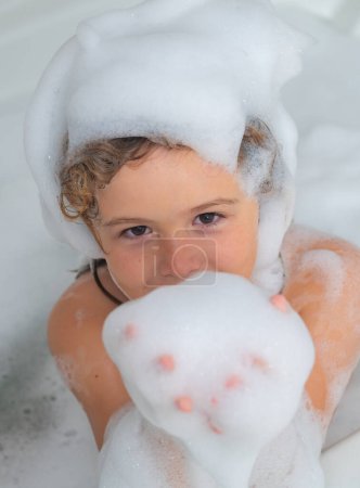 Téléchargez les photos : Petit enfant dans une baignoire. Lavage dans le bain. Enfant avec de la mousse de savon sur les cheveux prenant un bain. Portrait rapproché d'un enfant souriant, des soins de santé et de l'hygiène des enfants. Baignoire avec bulle de savon - en image libre de droit