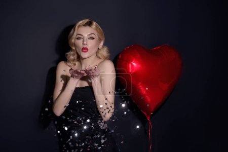 Téléchargez les photos : Femme blonde sexy soufflant des confettis. Femme amoureuse du cœur. Belle jeune femme tenant des ballons de coeur rouge, Saint Valentin. Un rencard romantique. Femme célébrant la Saint-Valentin - en image libre de droit