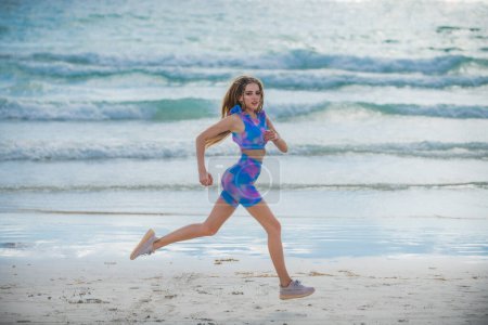 Téléchargez les photos : Femme qui court jogging sur la plage. Fit femme faisant de l'entraînement sur la plage d'été de sable de mer. Sport d'été. Fitness femme sport modèle jogging style de vie. La course. Fit girl courir sur la plage - en image libre de droit
