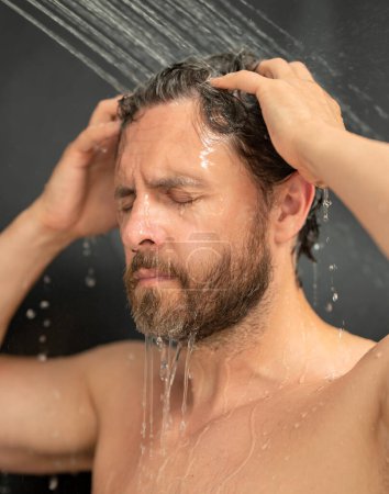 Foto de Millennial hombre lavando el cabello en el baño. Cabezal de ducha en la bañera. Cara en espuma en la ducha. Bañista duchándose. Un tipo de cerca duchándose. Concepto ducha. El hombre está bajo las gotas de agua en las duchas - Imagen libre de derechos