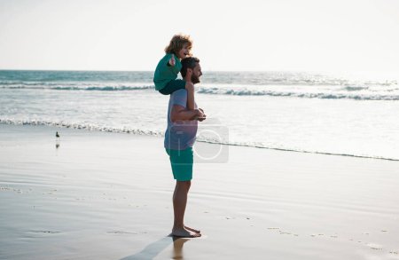Foto de Papá y el niño caminando juntos en la playa de verano. Un niño pequeño con papá cargándolo en hombros. Papá y el niño disfrutando al aire libre. Estilo de vida y vacaciones familiares, concepto de hombres de felicidad - Imagen libre de derechos