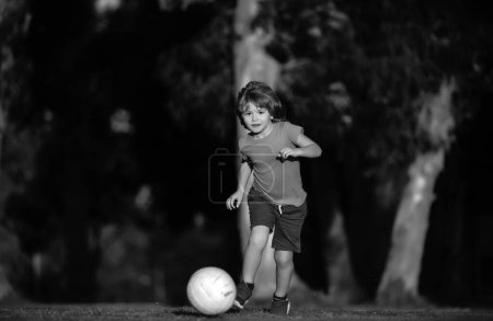 Téléchargez les photos : Enfant garçon jouant au football sur le terrain de football. Un gamin qui joue au foot. Enfant footballeur dans le parc - en image libre de droit