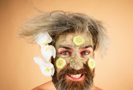 Foto de Hombre divertido con máscara de arcilla y rodajas de pepino en la cara. Hombre con máscara hidratante cosmética, fondo de estudio aislado. Cuidado facial masculino - Imagen libre de derechos