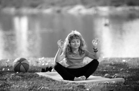 Photo for Little child sitting on the roll mat practicing meditate yoga in the park outdoor. Kid boy practicing yoga pose, lotus pose yoga - Royalty Free Image