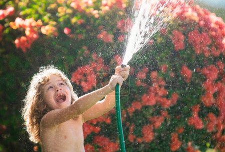 Photo for Cute boy watering plants in the garden at summer day. Child with garden tools and watering hose in backyard garden. Kid having fun on yard. The concept of child kindness and childhood - Royalty Free Image