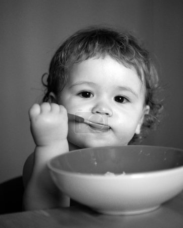Photo for Portrait of cute Caucasian child kid with spoon. Hungry messy baby with plate after eating puree - Royalty Free Image