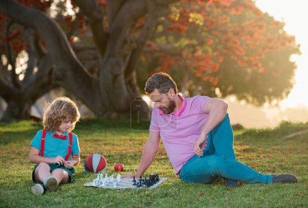 Téléchargez les photos : Père et fils jouant aux échecs passent du temps ensemble dans le parc. Enfants école d'échecs - en image libre de droit