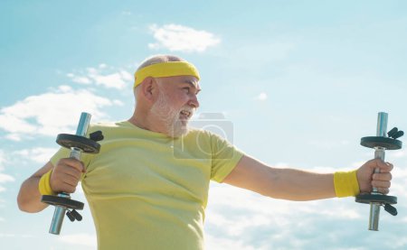 Photo for Senior sportsman in sport center. Lifting dumbbells. Body care and healthcare. Senior man exercising on blue sky. Healthcare cheerful lifestyle - Royalty Free Image