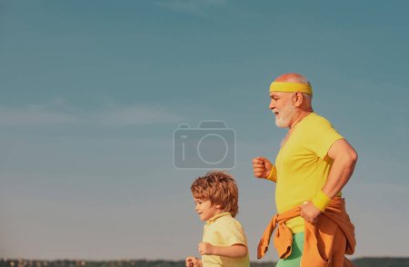 Téléchargez les photos : L'âge n'est pas une excuse pour relâcher votre santé. Homme âgé avec enfant mignon pratiquant le sport sur fond de ciel bleu. Grand-père et petit-fils courent - en image libre de droit