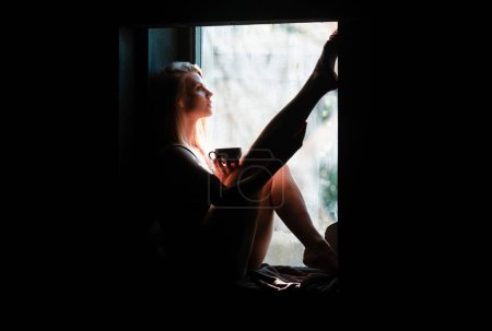 Téléchargez les photos : Sensuelle fille posant sur près de fenêtre boire du café. Belle jeune femme, matin ou soir - en image libre de droit