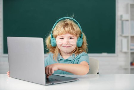 Photo for Happy boy in headphones watch video lesson on computer in school, child in earphones have online lesson, using laptop - Royalty Free Image
