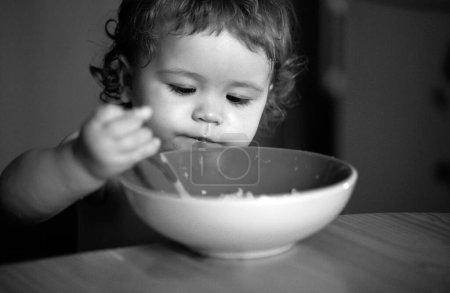 Photo for Funny little baby in the kitchen eating with fingers from plate - Royalty Free Image