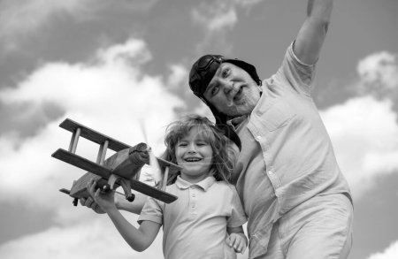 Téléchargez les photos : Petit-fils drôle enfant et grand-père jouant avec avion en bois sur fond de ciel d'été. Enfant garçon avec des rêves de voler ou de voyager - en image libre de droit