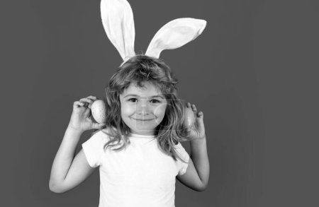 Foto de Feliz Pascua. Niño en orejas de conejo cazando huevos de Pascua aislados sobre fondo azul - Imagen libre de derechos