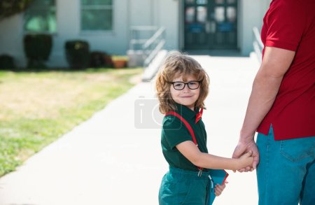 Photo for Father and son walking trough school park. Portrait of happy nerd pupil holding teachers hand - Royalty Free Image