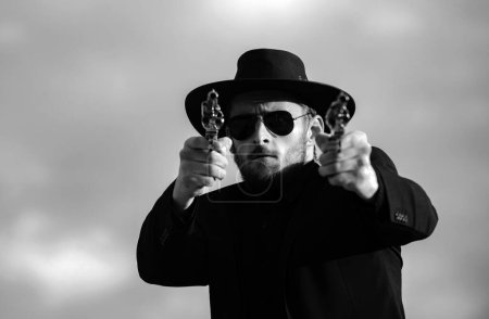 Sheriff in black suit and cowboy hat shooting gun, close up western face. Sheriff or cowboy in black suit and cowboy hat. Man with west vintage pistol revolver gun and marshal ammunition