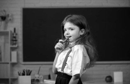 Photo for Cute child eating chocolate sweets at school. Kid is learning in class on background of blackboard - Royalty Free Image