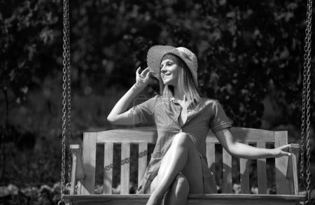 Foto de Mujer despreocupada disfrutar del verano. Retrato de mujer joven atractiva en sombrero de paja al aire libre en verano día soleado balanceo en un columpio en el patio trasero - Imagen libre de derechos