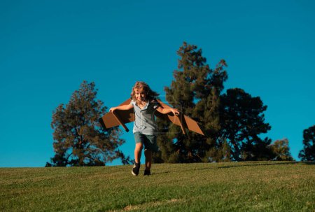 Foto de Niño caucásico jugando con avión de juguete en el fondo del cielo afuera en la colina de verano cubierta de hierba. Soñar con un concepto de futuro feliz - Imagen libre de derechos