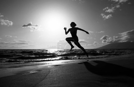 Foto de Silueta de mujer corredora ejercitándose en correr sprint ejercitándose en jogging de playa, actividad saludable al aire libre - Imagen libre de derechos
