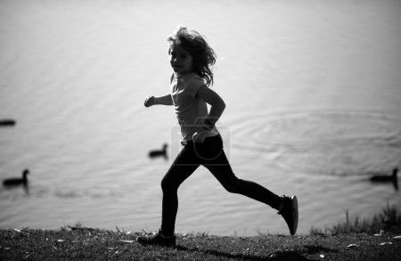 Foto de Niños corriendo al aire libre. Carrera y deporte saludable para los niños. Niño corriendo en el campo de verano cerca del lago, los niños fitness. Ejecutar entrenamiento al aire libre, correr por la mañana. Niños deportistas - Imagen libre de derechos