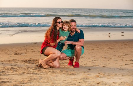 Téléchargez les photos : Bonne famille et enfant profitant du coucher de soleil sur la plage. Loisirs d'été - en image libre de droit