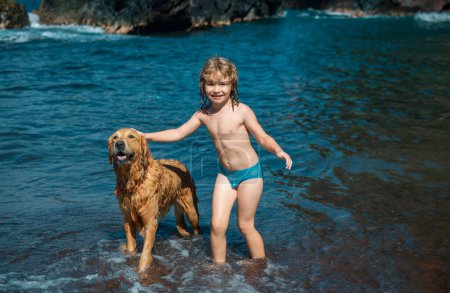 Foto de Niño jugando con perro en agua de mar en la playa - Imagen libre de derechos