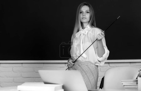 Téléchargez les photos : Professeur pointant sur la leçon. Jeune femme mignonne avec pointeur enseignant près du tableau noir - en image libre de droit