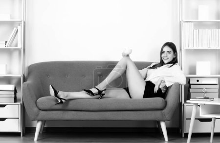 Mujer de negocios sexy con piernas sexy beber café. Mujer seductora, secretaria sensual sentarse en el sofá en la oficina