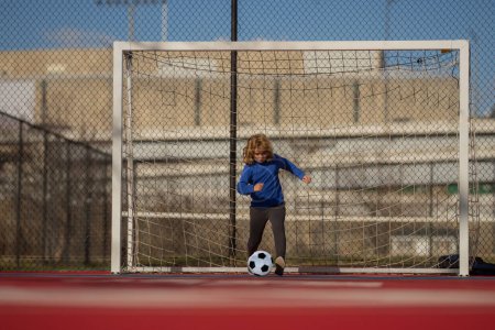 Child boy football or soccer player in action on football stadium kicking football ball for goal. Concept of sport, competition. Kid kick football ball. Kid kicking soccer ball. Sport for kids