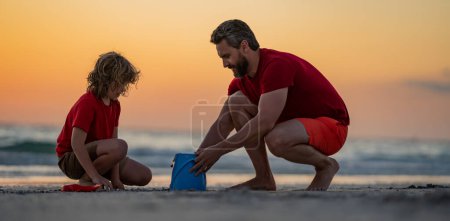 Téléchargez les photos : Père et fils enfant construisent un château de sable à la plage d'été, Kid et père construisent un château de sable. Père et enfant fils jouent sur la plage. Père et fils jouant dans le sable sur la plage tropicale au coucher du soleil - en image libre de droit