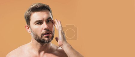 Beauty portrait of handsome man with moisturizing cream on face, isolated background. Skincare routine concept. Male beauty. Shaving, hair styling. Banner for header, copy space