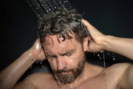 Téléchargez les photos : Homme millénaire laver les cheveux dans le bain. Pommeau de douche dans la baignoire. Visage en mousse dans la douche. Un baigneur prend une douche. Douche de gros bonnets. Concept de douche. L'homme est sous les gouttes d'eau dans les douches - en image libre de droit
