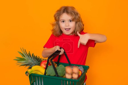 Photo for Shopping grocery. Portrait of child with grocery shopping cart. Kid with shopping basket, isolated on yellow studio background - Royalty Free Image