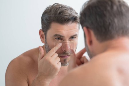Close-up portrait of perfect brunet man touching chin and skin. Handsome man touching face in front of the mirror in bath. Perfect skin. Man cosmetic, skin treatment. Hygiene and skin care male face